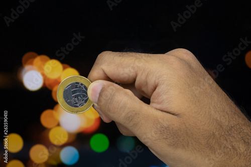 Holding a Brazilian money coin at a blurry background