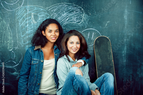 back to school after summer vacations, two teen real girls in classroom with blackboard painted together, lifestyle mixed races people concept close up