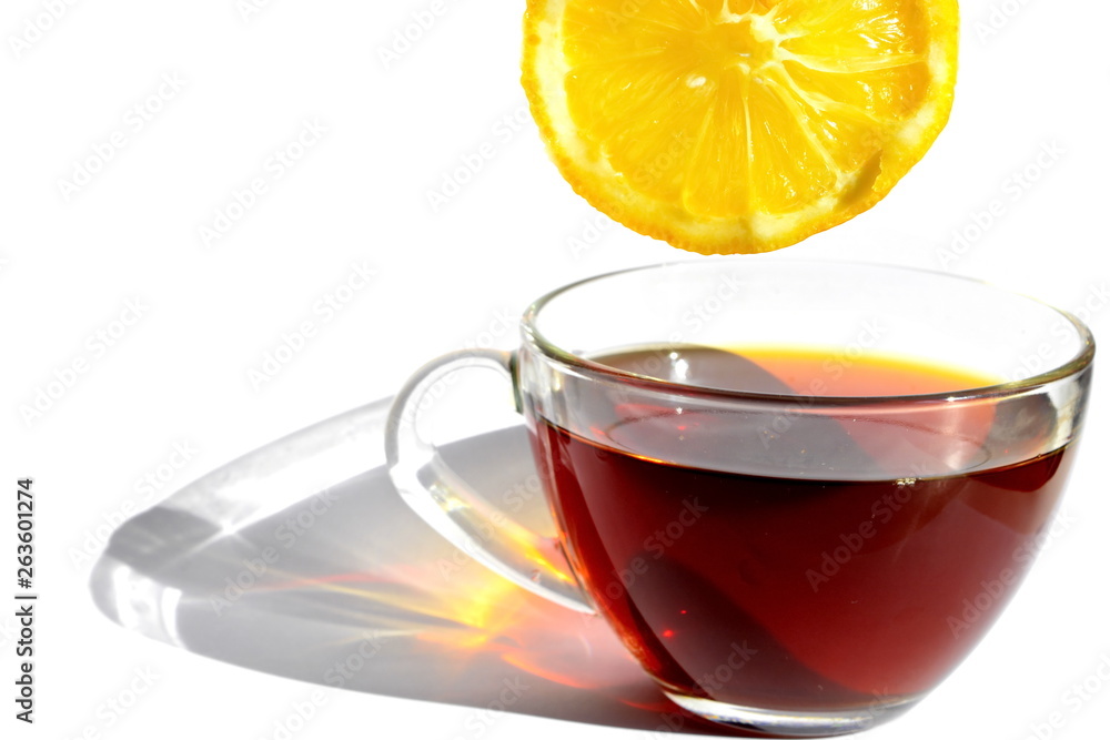 Transparent glass cup of hot black tea with long rainbow shadow in morning rays of sunlight and yellow slice of bitter sour lemon on white background. Isolated Transparent glass cup of hot black tea with long rainbow shadow in morning rays of sunlight and yellow slice of bitter sour lemon on white background. Isolated