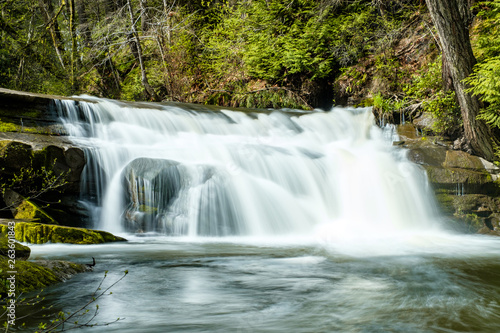 small beautiful waterfall inside forest in the park  with moss covered rocks and green trees on the surrounding area.