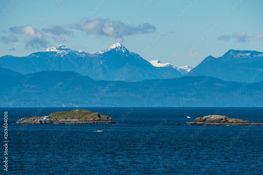 small island in the middle of blue ocean with snow covered mountain range in the background on a sunny day