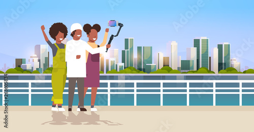 casual people using 3-axis gimbal stabilizer selfie stick for smartphone happy african american tourists taking photo standing together over cityscape background horizontal full length