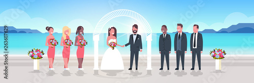 just married bride and groom with bridesmaids groomsmen standing together on sea beach near arch wedding ceremony concept sunrise mountains background full length horizontal