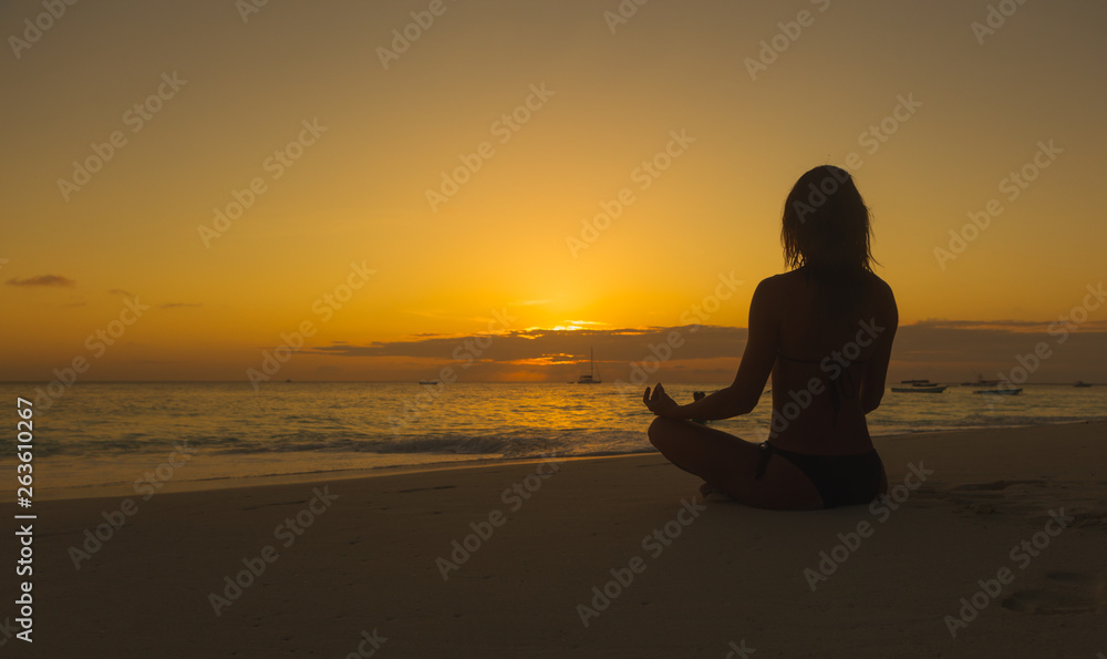 Women do meditation on the ocean beach at sunset