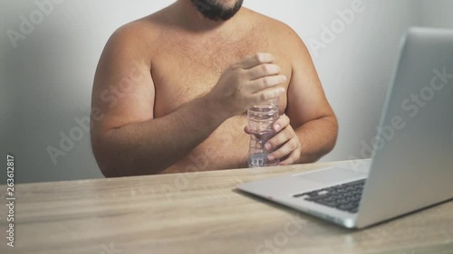 man sits at a computer and opens a bottle of water, imitating frictions. concept of strange people.