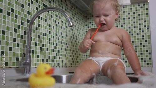 Cute toddler girl brushing her teeth in the bathroom. Cute baby sitting in the sink. 
