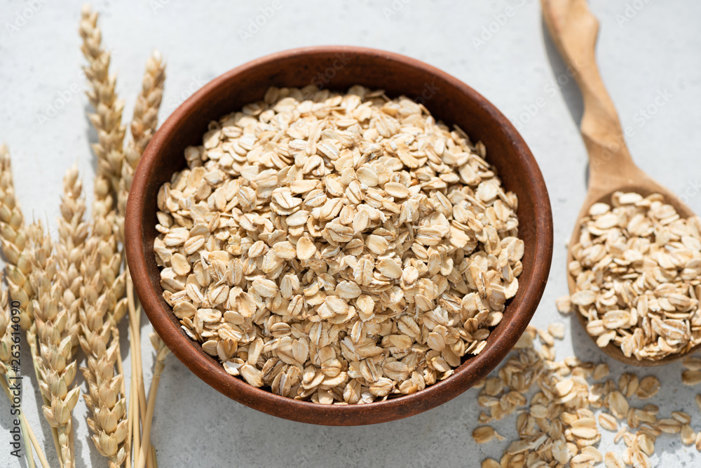 Rolled oats or oat flakes in bowl on concrete background. Closeup view. Healthy eating, healthy lifestyle, dieting and weight loss food concept Rolled oats or oat flakes in bowl on concrete background. Closeup view. Healthy eating, healthy lifestyle, dieting and weight loss food concept