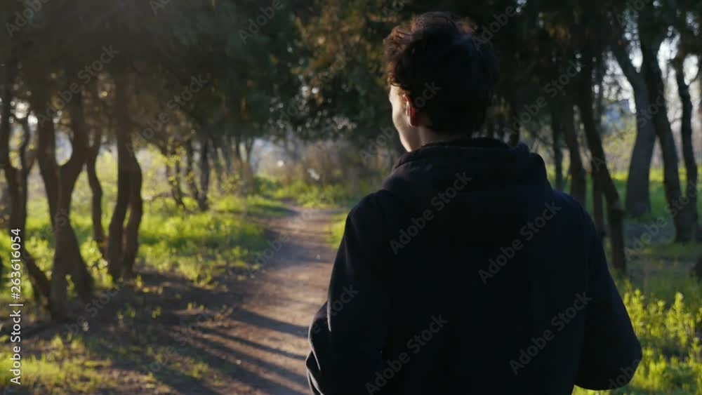 Young fit man in black jacket running in the beautiful park on sunset. Green grass and trees trunks on background. Slow motion Young fit man in black jacket running in the beautiful park on sunset. Green grass and trees trunks on background. Slow motion