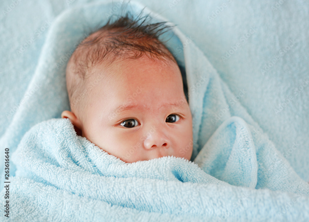 Portrait of Infant baby boy in towel roll looking at camera lying on bed after bath. Above view. Portrait of Infant baby boy in towel roll looking at camera lying on bed after bath. Above view.