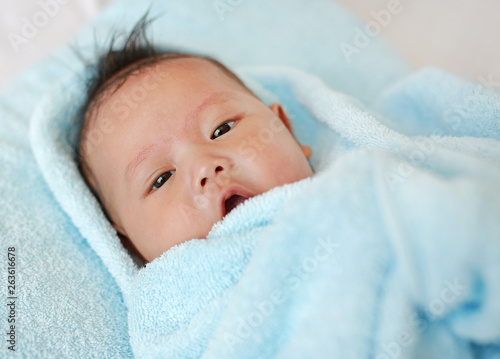 Happy infant baby boy in towel roll lying on bed after bath.