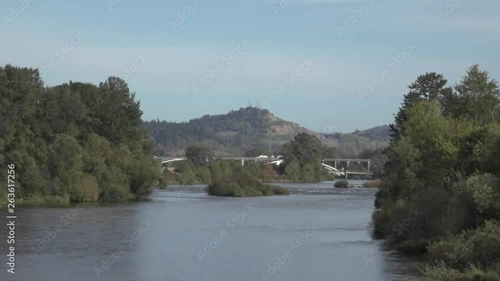 A wide angle view of the Willamette River cutting between forested river banks, flowing toward a highway bridge in the distance. A wide angle view of the Willamette River cutting between forested river banks, flowing toward a highway bridge in the distance.