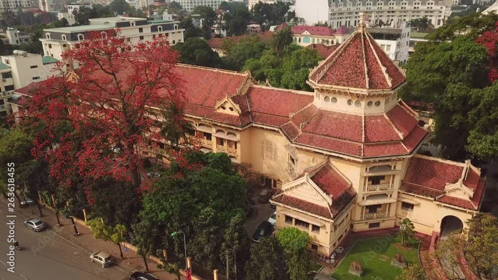 Aerial forward close-up tower National Museum Vietnamese History among blooming red exotic trees Hanoi Vietnam. Unique culture art colonial city. Cupola shaped edifice shape of pagoda Sight Travel Aerial forward close-up tower National Museum Vietnamese History among blooming red exotic trees Hanoi Vietnam. Unique culture art colonial city. Cupola shaped edifice shape of pagoda Sight Travel