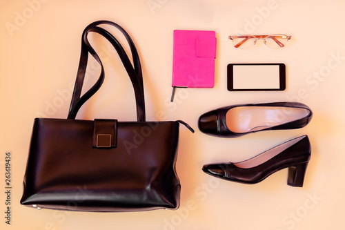 Black leather bag, black shoes, smartphone and glasses on pastel background.