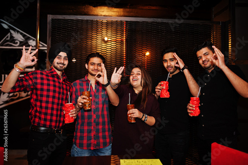  Group of indian friends having fun and rest at night club, drinking cocktails and show ok fingers together.