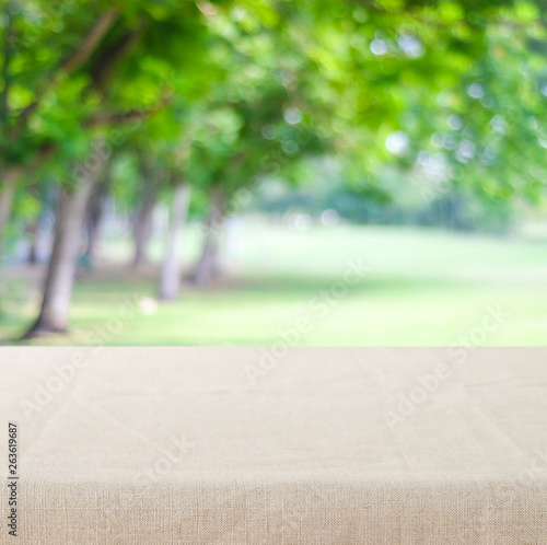 Empty table with linen tablecloth over blur green tree nature park outdoor background, product display montage, spring and summer season