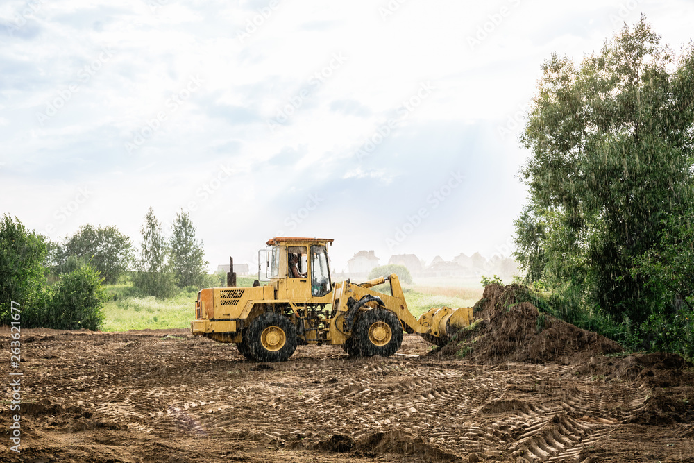 Fototapeta large yellow wheel loader aligns a piece of land for a new building. May be cut to banner or wallpaper with copy space.