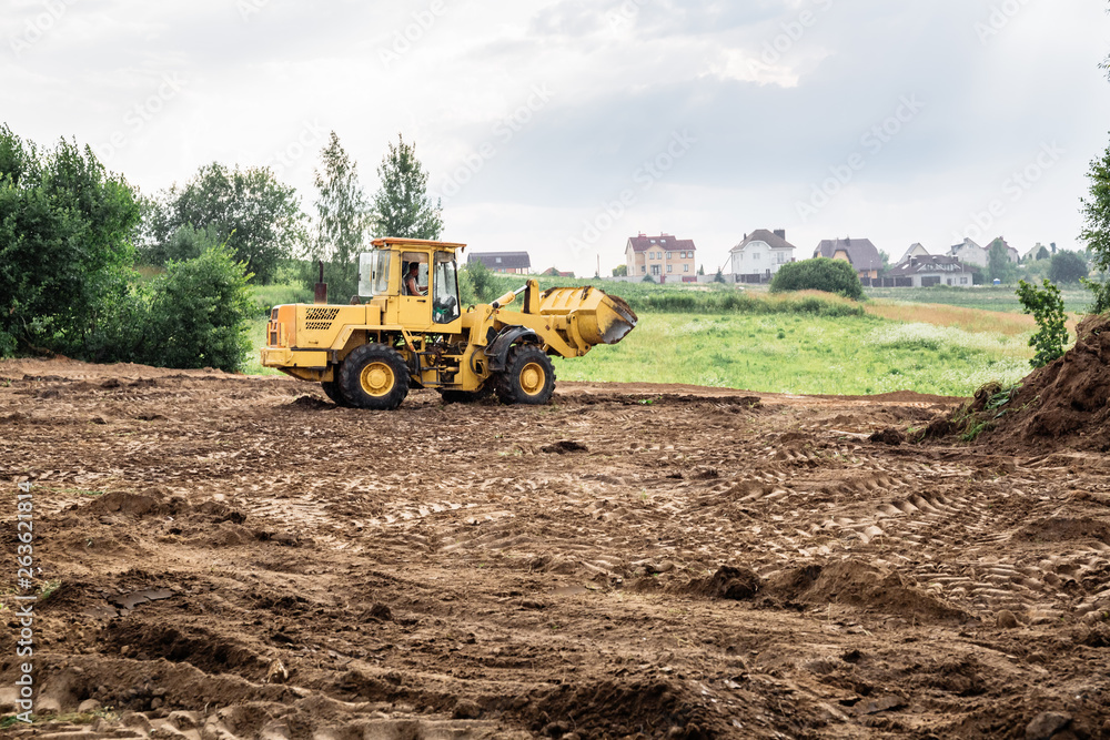 Fototapeta large yellow wheel loader aligns a piece of land for a new building