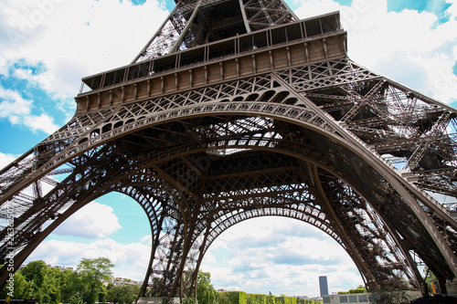 Low angle shot of the base of iconic Eiffel Tower on a spring summer day with blue sky and white clouds. Tourists consider Paris as the world's most romantic city and Eiffel tower most visited place  © PhotographrIncognito