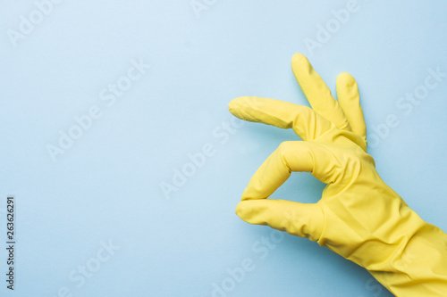 Hand in yellow gloves for cleaning on blue background. Home cleaning concept. Top view, copy space.