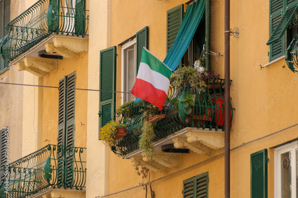 Balcony with flowers and Italian flag, house facade, Italy