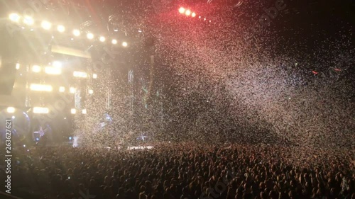 Crowd of people standing in concert hall under flashing and falling paper rain