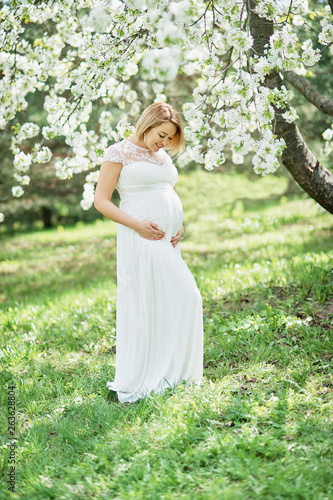 Spring mood, beautiful pregnant woman smell flowering cherry tree, enjoying nature, white floral garden.