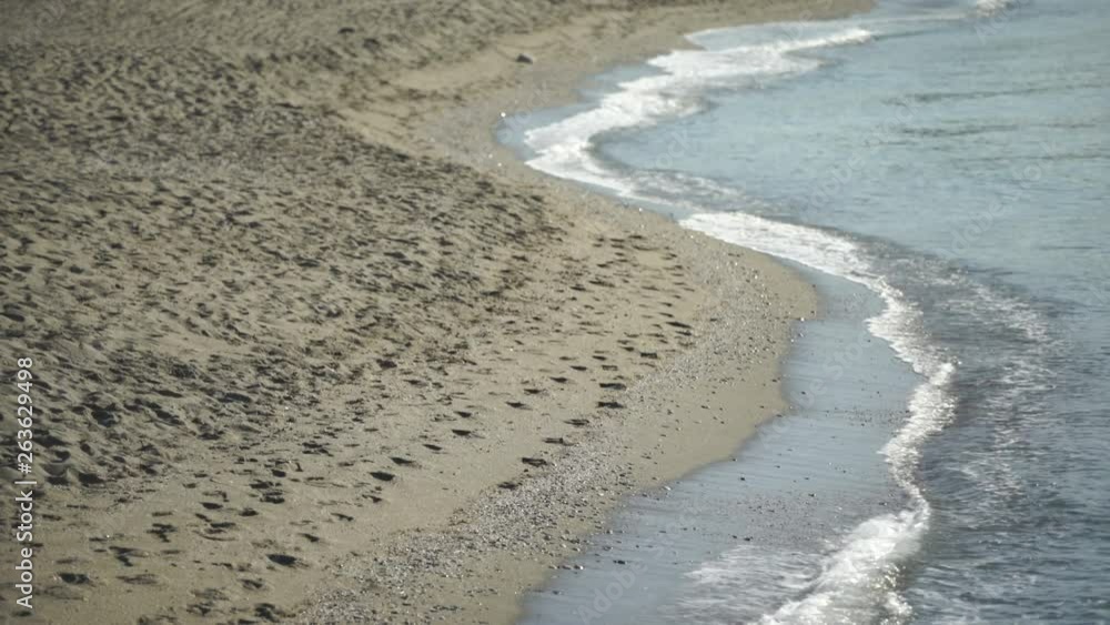 Waves gently washing up on sandy beach with pebbles and footsteps, waves wash against the shoreline 4K Waves gently washing up on sandy beach with pebbles and footsteps, waves wash against the shoreline 4K