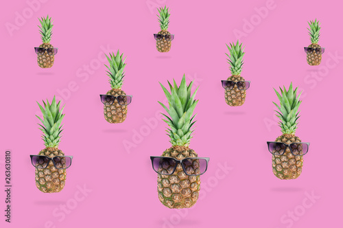 Lot of fresh whole pineapples with green leaves and black sunglasses lying on pink table on kitchen. Top view. Cooking concept