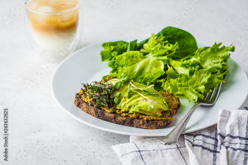 Avocado toast with pesto, sprouts and salad on white plate.