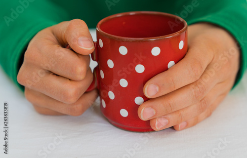 woman holding a red coffee cup with white polka dots on a white table cloth