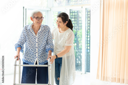 Asian young woman helping senior woman in using walker during rehabilitation, close up of carer supporting her elderly grandmother with walking and exercising at home photo