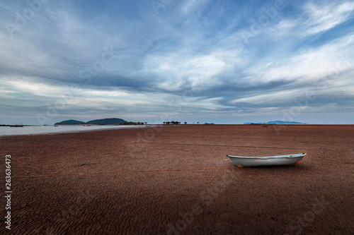 Tropical landscape with boat on the dry beach with the background is the sea and mountain on blue sky at Chumphon Thailand