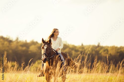 Young girl goes sorrel horse riding in field