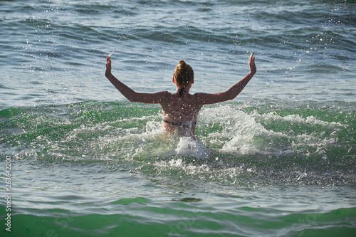 Summer lifestyle portrait of pretty young girl having fun on a tropical beach, splashing sea water