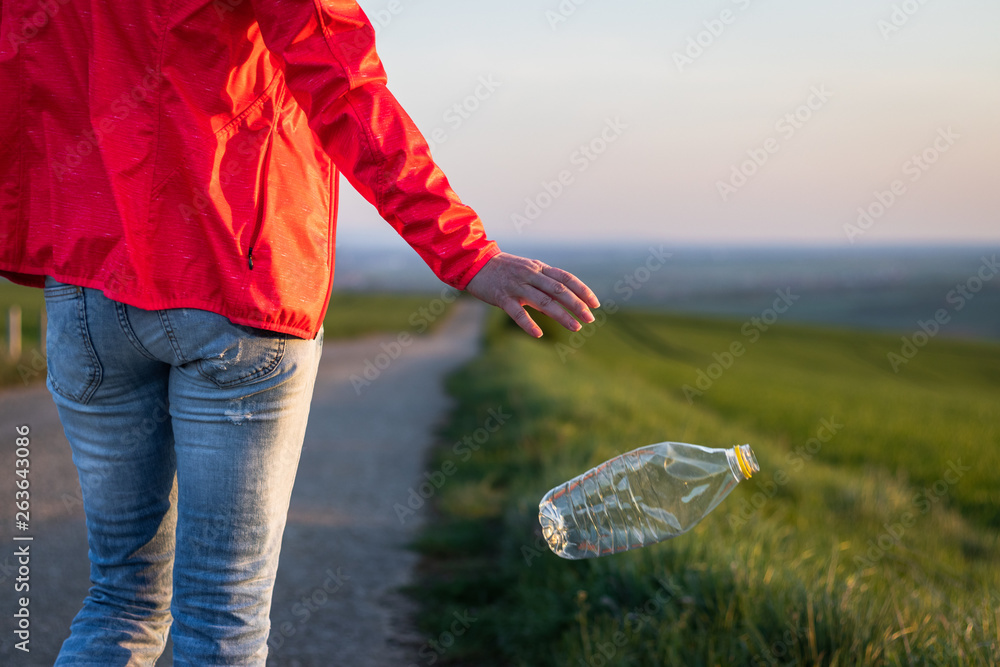 Hand throwing away plastic bottle in nature. Environmental damage by