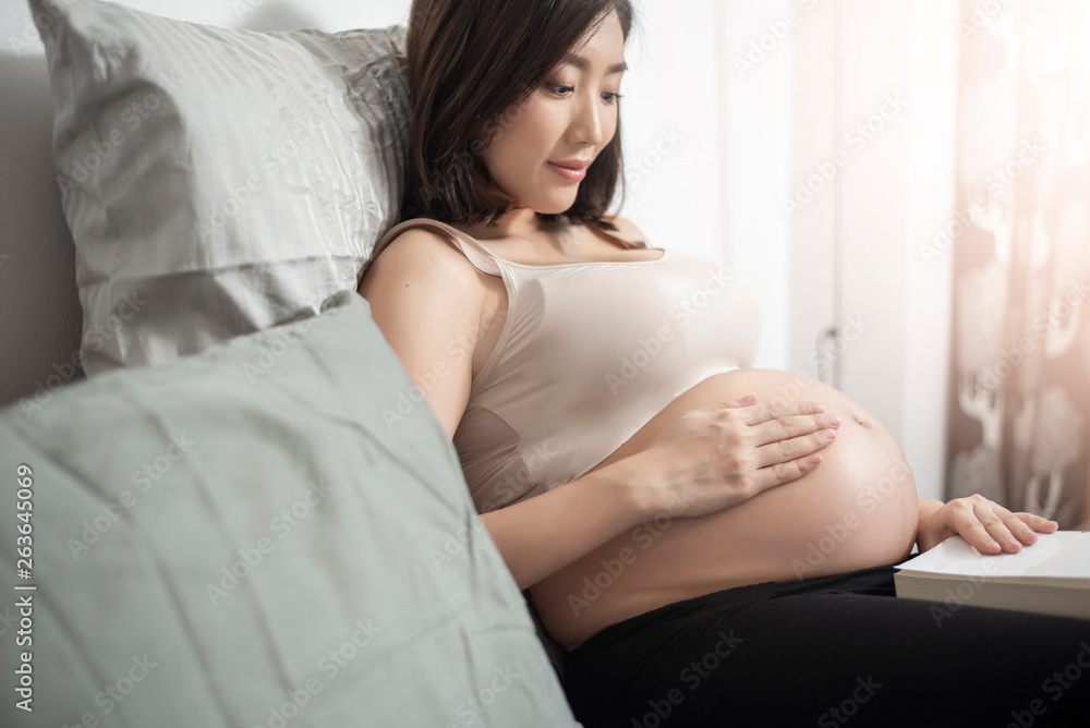 Beautiful asian pregnant woman lying on her bed and reading a book Beautiful asian pregnant woman lying on her bed and reading a book