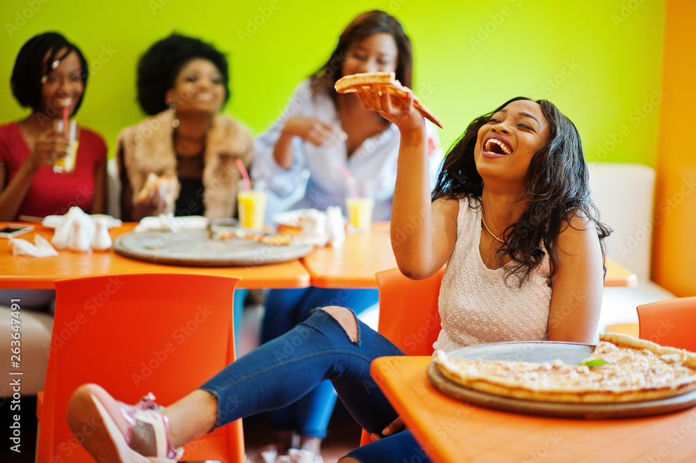 African woman with pizza sitting at restaurant against dark skinned girls.