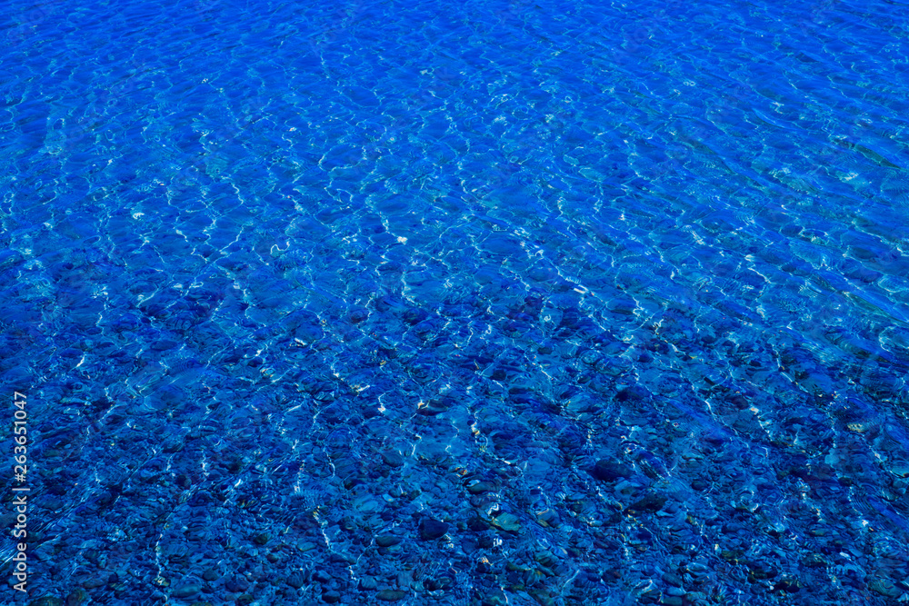 Obraz premium Blue water surface with ripples through which the sandy bottom with pebbles is visible