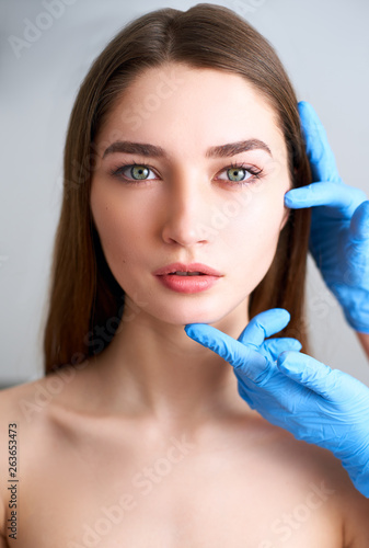 Beautician doctor s hands in gloves touching face of attractive woman. Fashion blonde model after cosmetic treatment. Aesthetic cosmetology  plastic surgery concept. Modern female beauty standard.