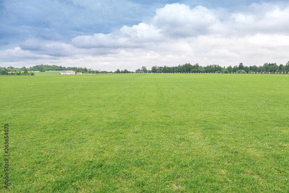 Rural landscape. The flat well-groomed field of a short-haired grass, a country house in the distance at the hill. The beautiful cloudy sky in sunny day Rural landscape. The flat well-groomed field of a short-haired grass, a country house in the distance at the hill. The beautiful cloudy sky in sunny day