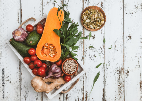 ingredients for vegetarian salad in wooden box with pumpkin, tomatoes, avocado, ginger root, garlic, pumpkin and sunflower seeds, arugula salad on white wooden background, top view, copy space photo