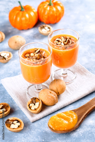 Healthy pumpkin smoothie with walnuts and cinnamon in glasses on rustic background