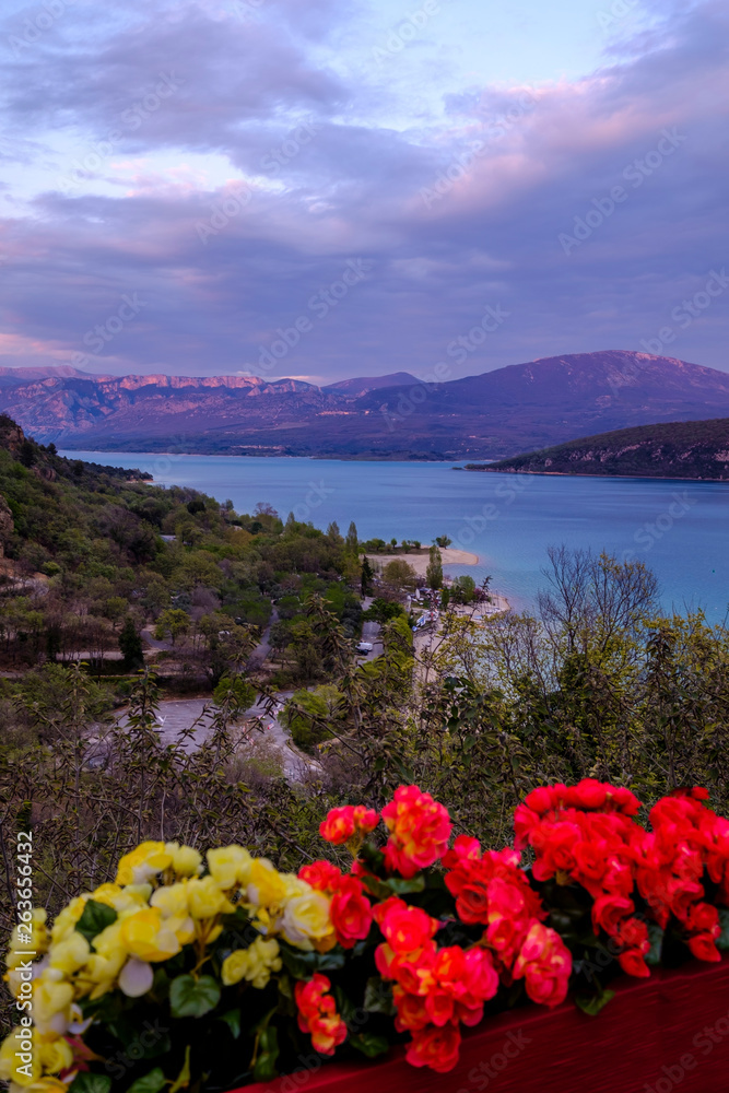 Vue panoramique sur le lac de Sainte-Croix au printemps. Coucher de soleil. Provence. France. Photo verticale. Fleurs rouges et jaunes au premier plan.