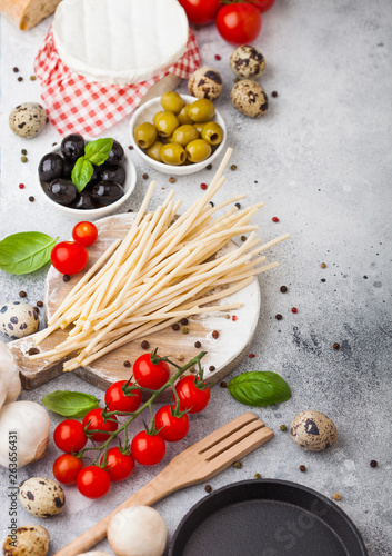 Homemade spaghetti pasta with quail eggs with bottle of tomato sauce and cheese on kitchen background. Classic italian village food. Garlic, champignons, black and green olives, pan and spatula.