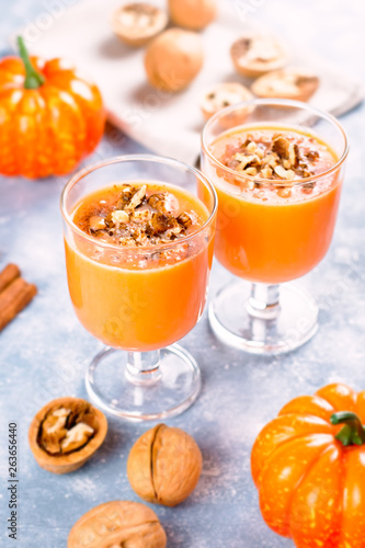 Healthy pumpkin smoothie with walnuts and cinnamon in glasses on rustic background