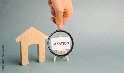 A poster with the word Taxation near a miniature wooden house. The concept of the tax burden on the property. Payment of taxes. Mortgage tax / Inspectorate. Housing. Apartment. Home photo