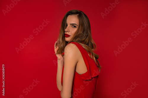 Close up inside studio portrait of adorable stylish woman with red lips and wearing red dress over isolated background 