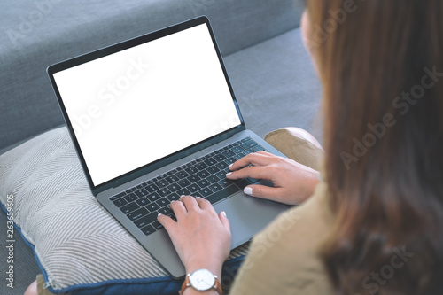 Mockup image of a woman using and typing on laptop keyboard with blank white screen while sitting in living room