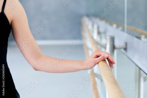 Ballerina is doing exercises in ballet modern school. Dancer is putting hand on barre by mirror. Girl has dance workout. Close up.