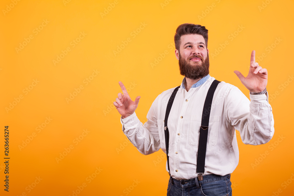 Cheerful bearded man smiling and pointing up over yellow background Cheerful bearded man smiling and pointing up over yellow background